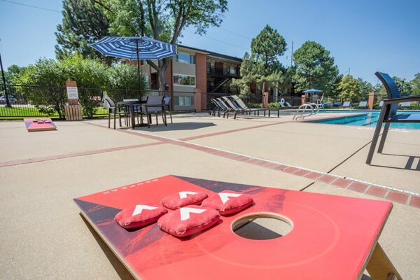 Pool area with lounge chairs, tables with umbrellas, and corn hole game.
