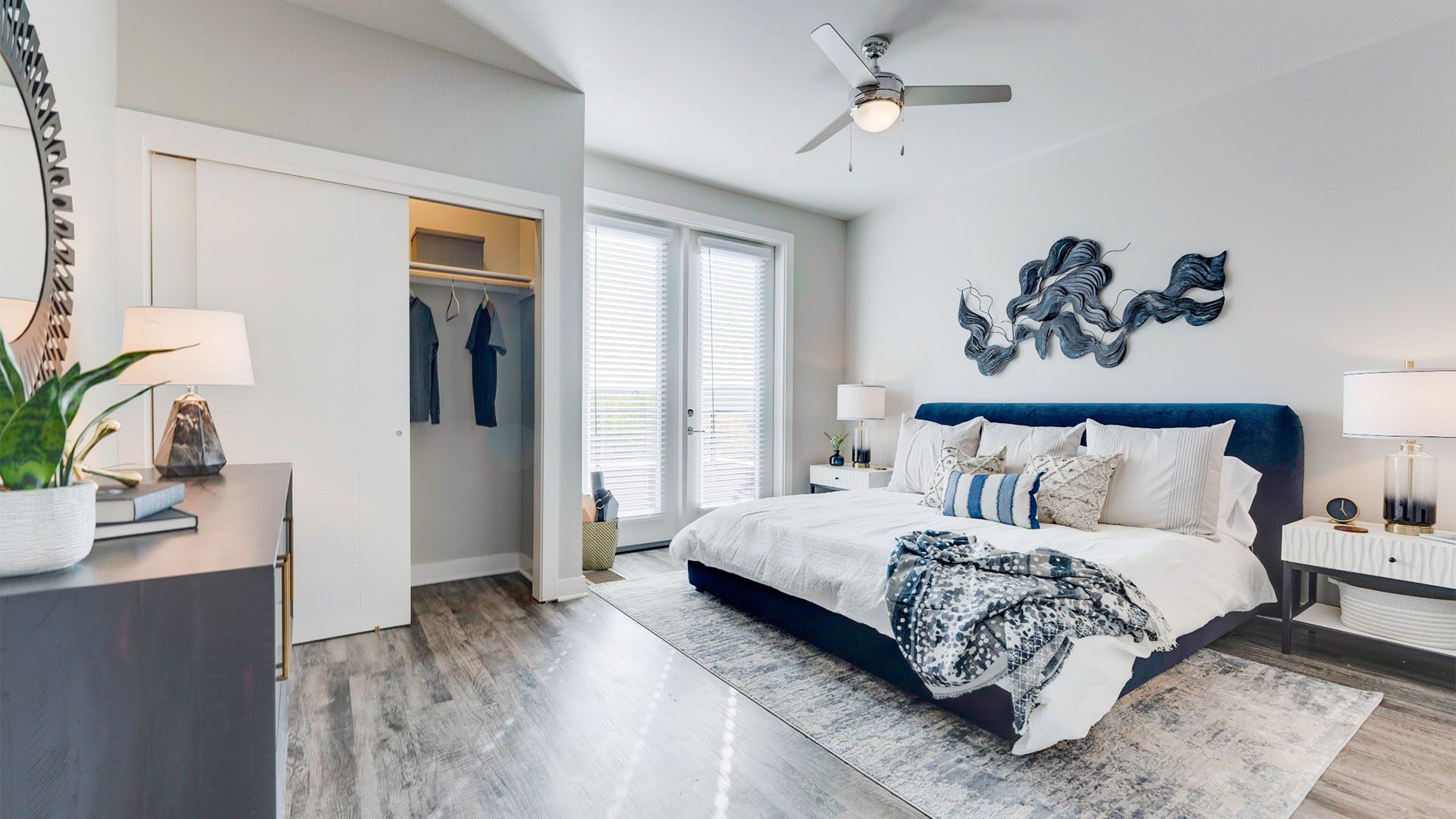 Bedroom with wood floor, rug, large bed with plush headboard, closet, and door to balcony.