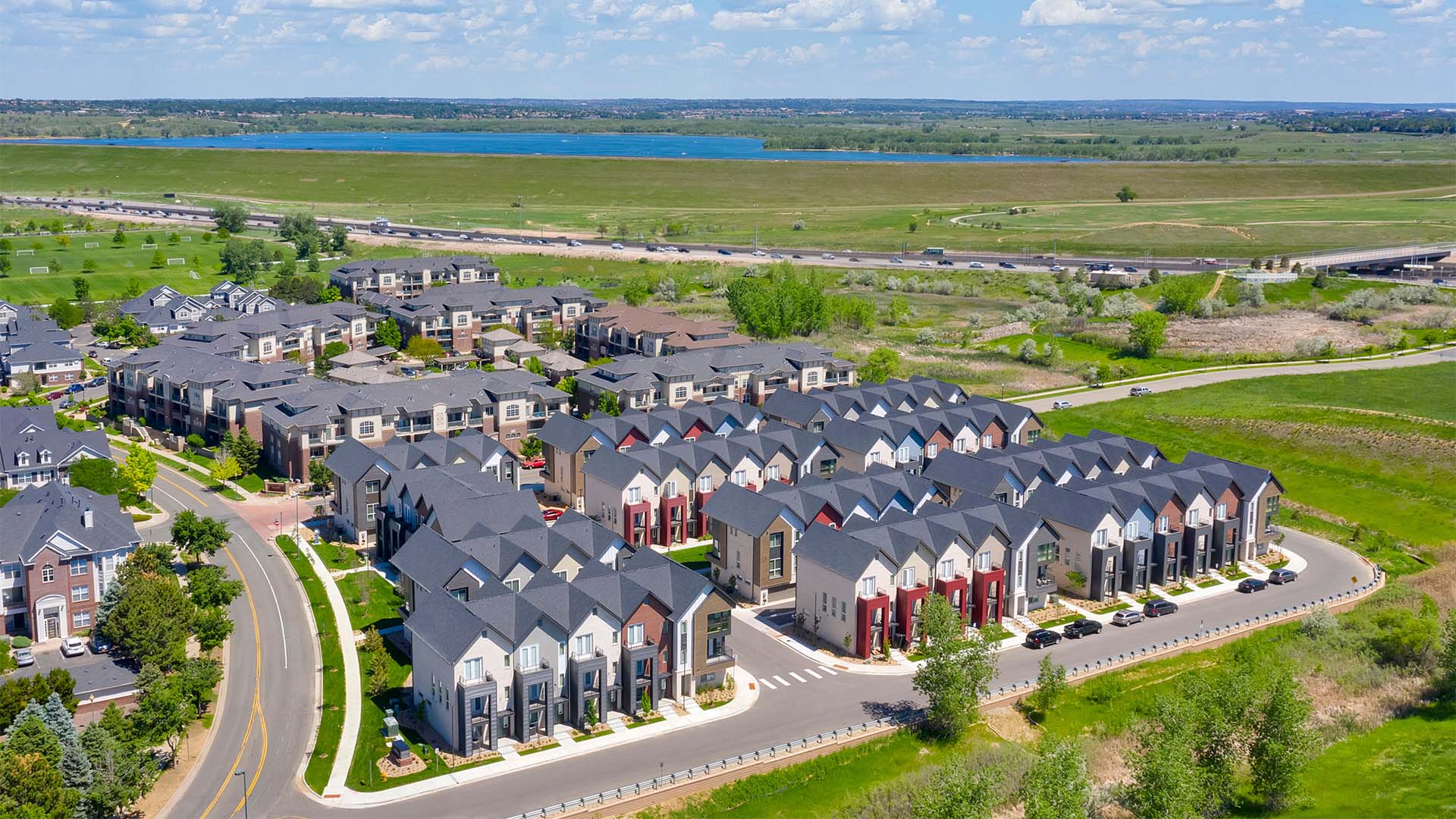 Aerial view of Dayton Station townhomes with balconies overlooking lush lawn and lake in the distance.