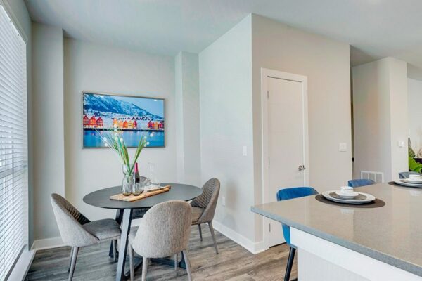 Dining area with round table, plush modern chairs, large window, and wintery photograph.