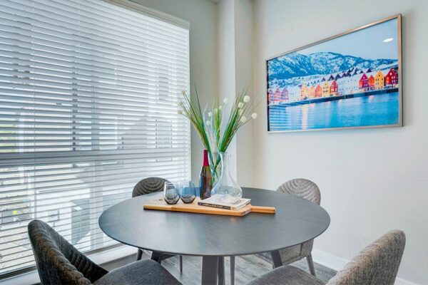 Dining area with round table, plush modern chairs, large window, and wintery photograph.