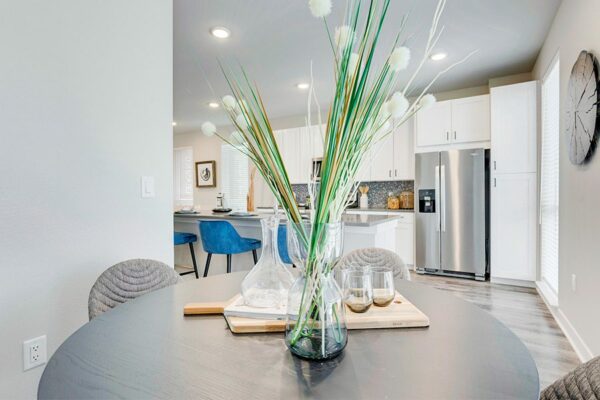 Detail of dining table with glass vase with grasses, charcuterie board with decanter and glasses, and kitchen behind.