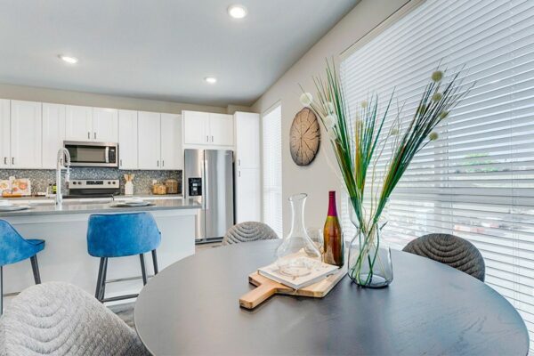 Kitchen and dining area with round dining table, island with stools, and large windows.