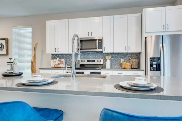 Detail of kitchen island with tan counters, modern place settings, and blue stools.