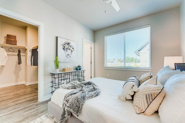 Bedroom with large bed with plush headboard, modern furniture and artwork, and doors to bathroom and large walk in closet.