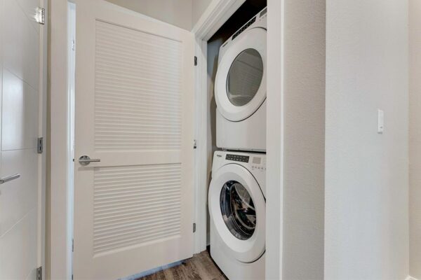 Laundry closet with slatted door and stacked washer and dryer.