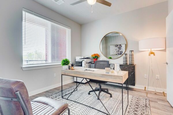 Office with modern furniture, round framed mirror, tripod floor lamp, and large window.