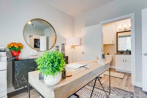 Office with modern furniture, round framed mirror, tripod floor lamp, and door to bathroom.