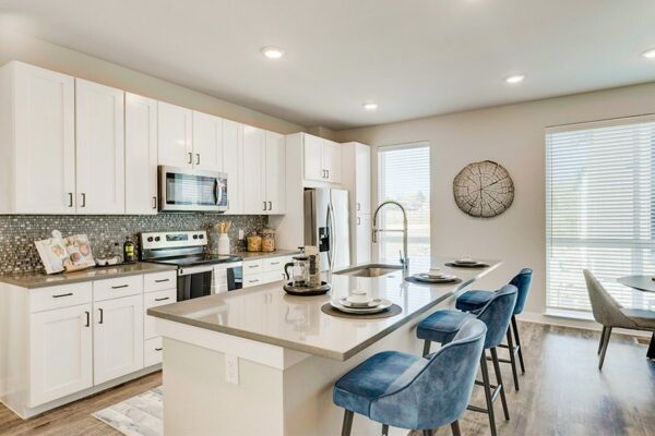 Kitchen with wood floor, white cabinets, tan counter, stainless steel appliances, and island with stools.