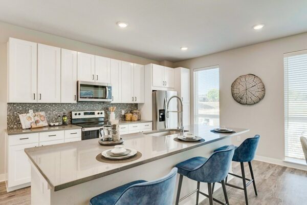Kitchen with wood floor, white cabinets, tan counter, stainless steel appliances, and island with stools.