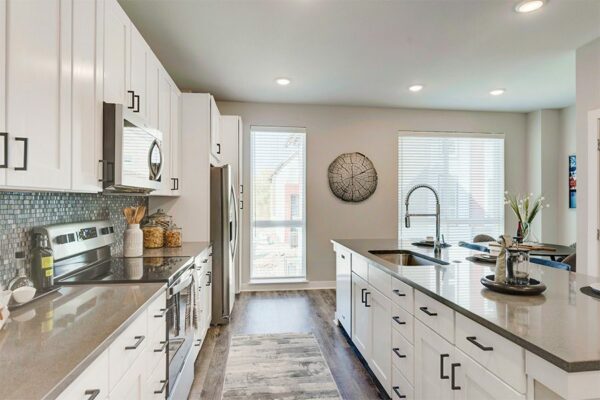 Kitchen with wood floor, white cabinets, tan counters, stainless steel appliances, and large windows.