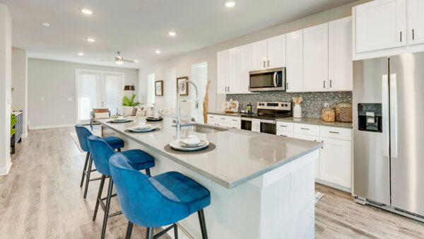 Kitchen with wood floor, white cabinets, tan counters, stainless steel appliances, and island with stools.