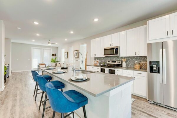 Kitchen with wood floor, white cabinets, tan counters, stainless steel appliances, and island with stools.