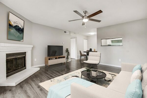 Living room with wood floor, plush sectional couch, modern furniture, ceiling fan, and fireplace.