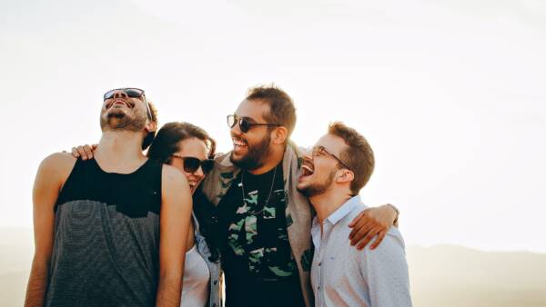 Friends laughing outside with arms around each other.