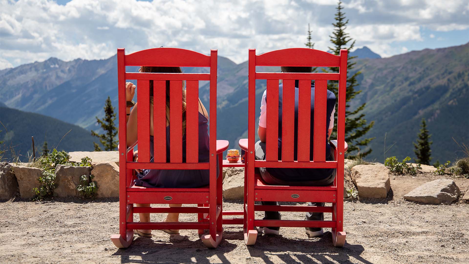 Friends sitting on mountaintop in large red wood chairs.