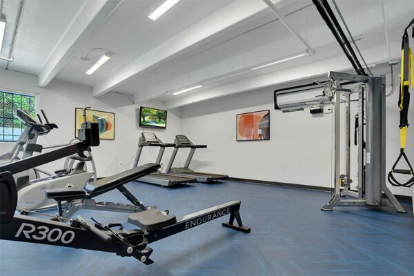 Fitness center with wall mounted TV, treadmills, elliptical machines, rower, and weight machine.