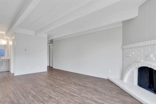 Living room with wood floor, grey walls, white brick fireplace, and door to bathroom..