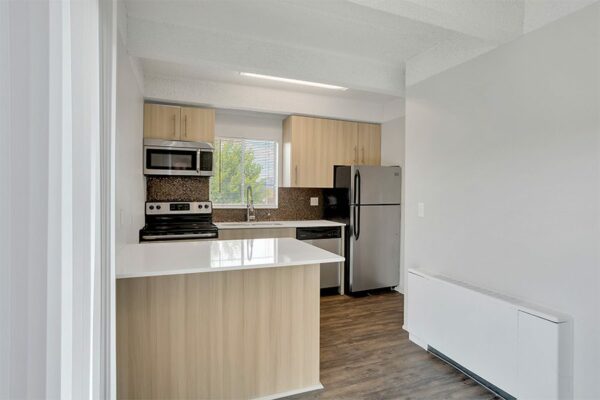 Kitchen with wood floor and cabinets, light counters, and stainless steel appliances.