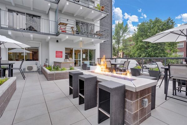 Patio with dining tables, fire pit, and BBQ grill overlooked by apartment balconies.