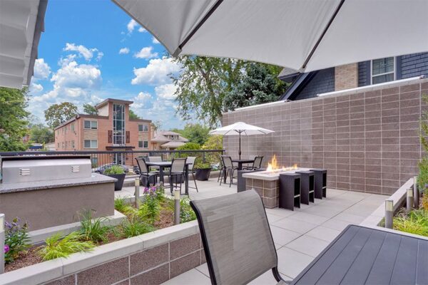 Patio with dining tables, umbrellas, fire pit, and lush planters.