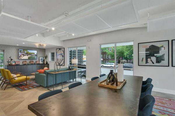 Lounge with large table, wall mounted TV, comfortable furniture, and modern abstract artwork.