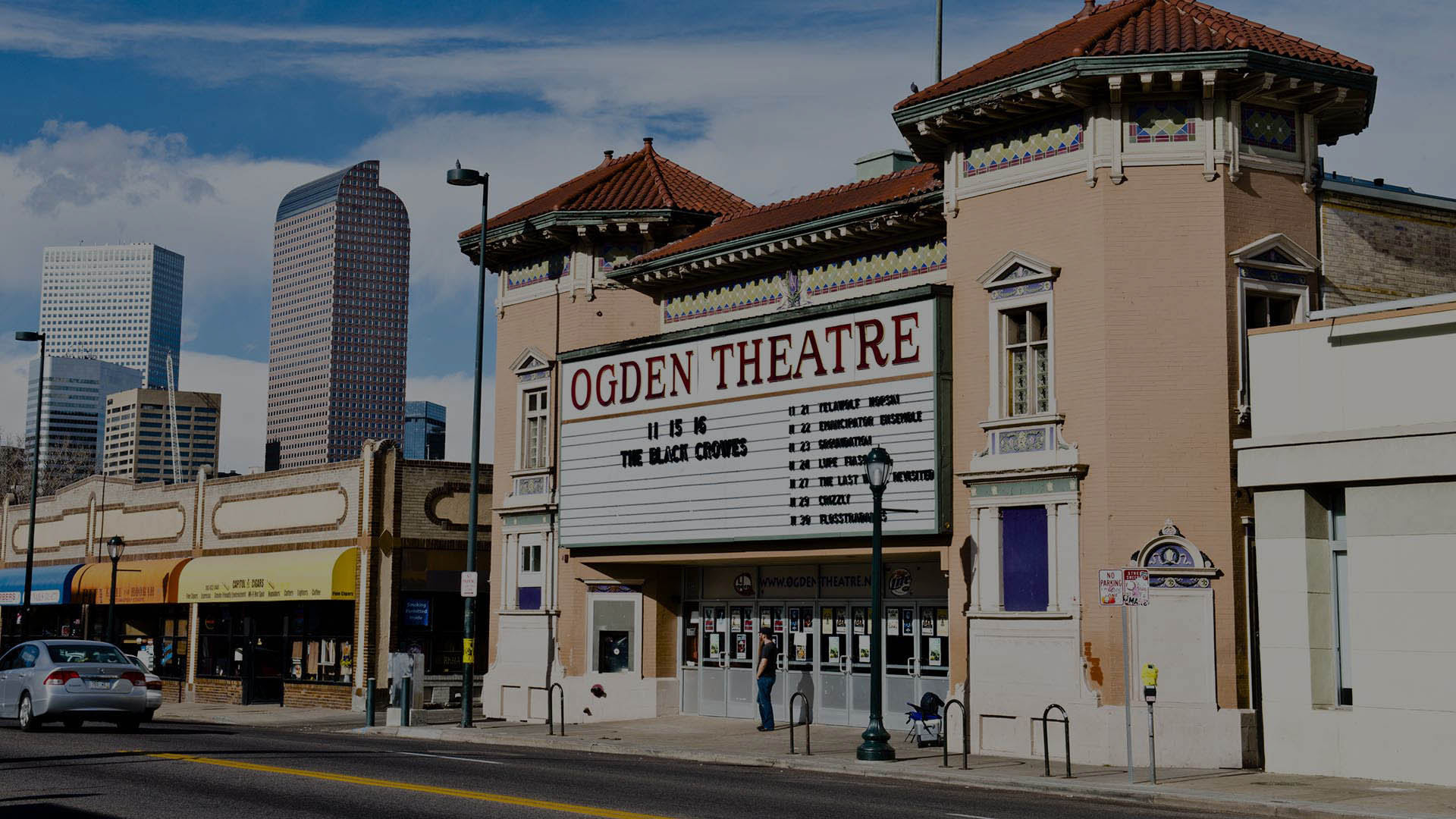 Ogden Theatre on Colfax in Denver with classic construction, large marquee sign, and Denver skyline behind.