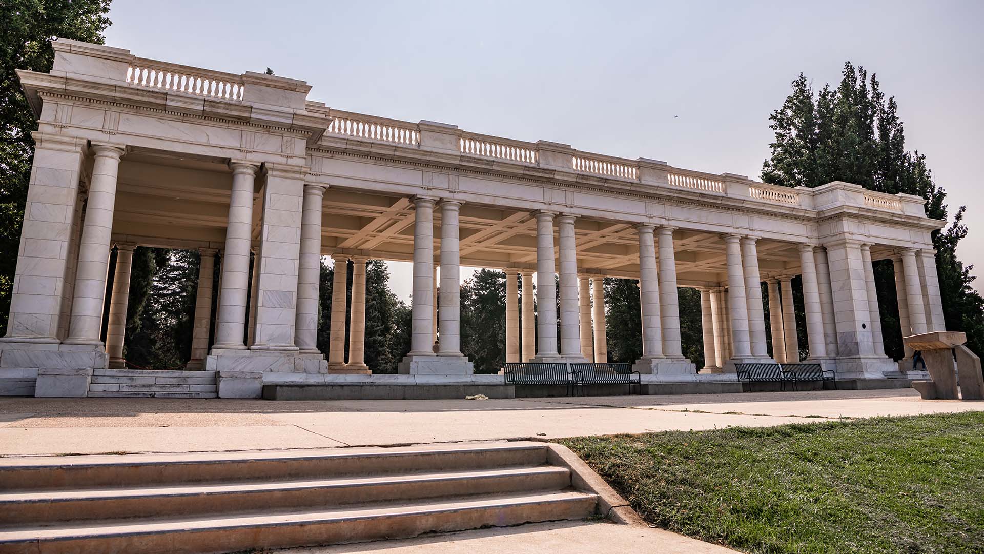 Stone pavilion at Cheeseman Park surrounded by lush lawns and tall trees.