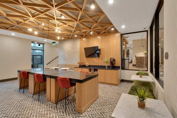Lounge with geometric tile, large stone table, tables with chairs, and wall mounted TV.