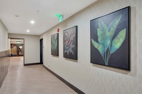 Hallway with wood floor, pattern wallpaper, and large paintings of plants.