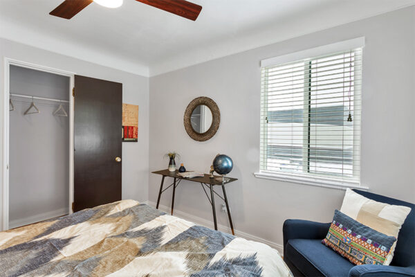 Bedroom with plush lounge chair, table with decor, ceiling fan, and large window.