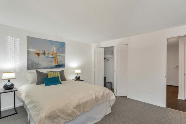 Bedroom with carpet, plush bed, modern bedside tables with lamps, and abstract artwork.