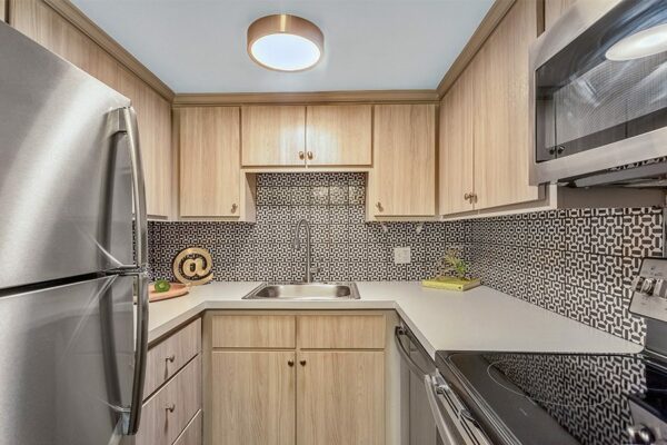 Kitchen with light cabinets and counters, stainless steel appliances, and tiled backsplash.