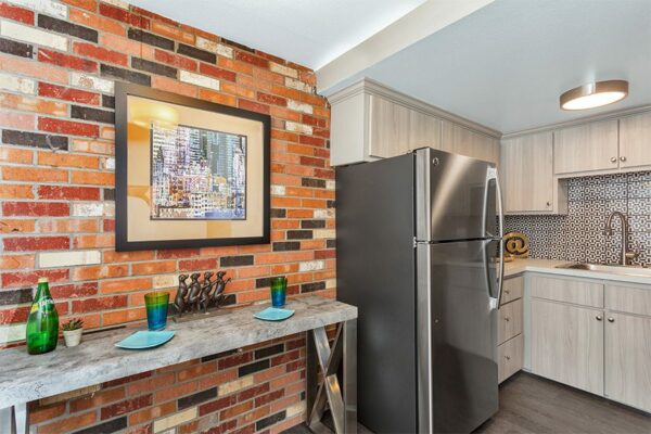 Kitchen with wood cabinets, light counters, stainless steel appliances, and brick accent wall with artwork.