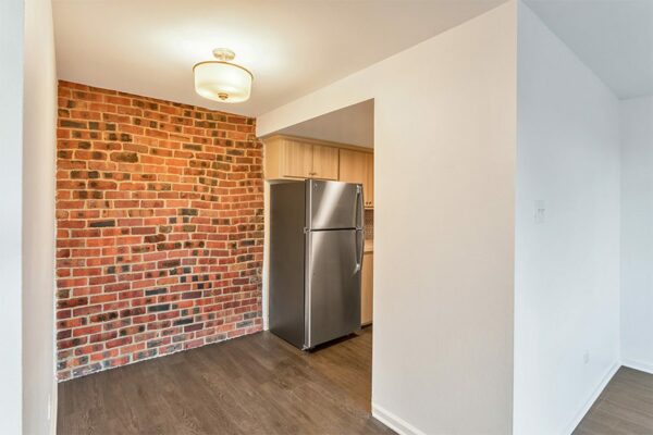 Dining area with wood floor, brick accent wall, and entry to kitchen.
