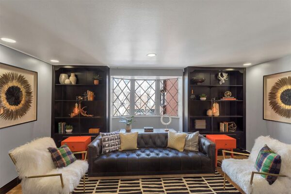 Lounge with plush furniture, built in shelves with eclectic decor, and large window.