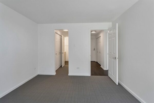Bedroom with carpet, cool grey walls, and doors to bathroom and hallway.