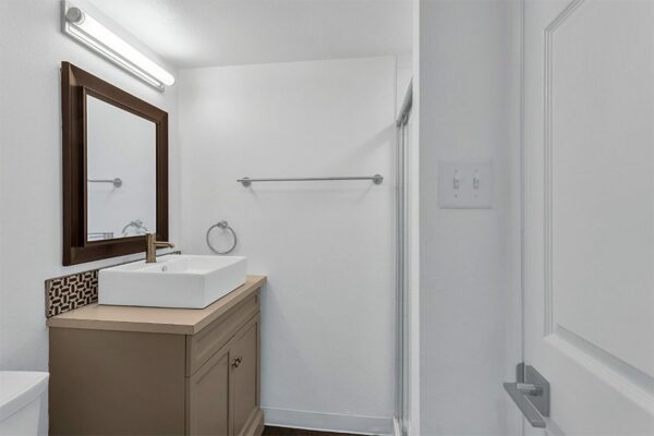Bathroom with wood cabinet, framed mirror, vessel sink, and glass shower door.