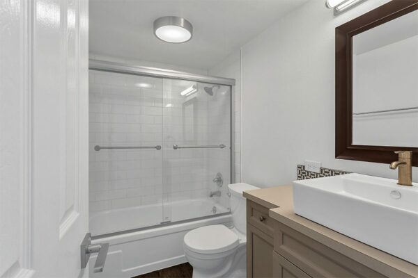 Bathroom with wood cabinet, vessel sink, framed mirror, and tiled shower tub with glass door.