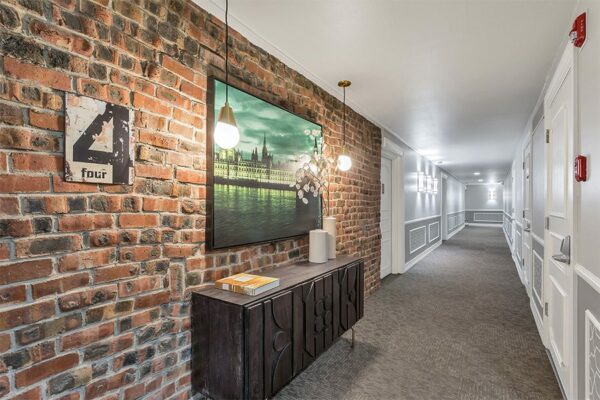 Apartment hallway with brick accent wall, brass pendant lights, and eclectic decor.