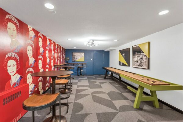 Game room with geometric carpet, pop art wallpaper, shuffleboard table, and bar tables.