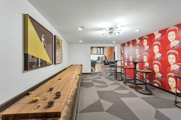 Game room with geometric carpet, pop art wallpaper, shuffleboard table, and bar tables.