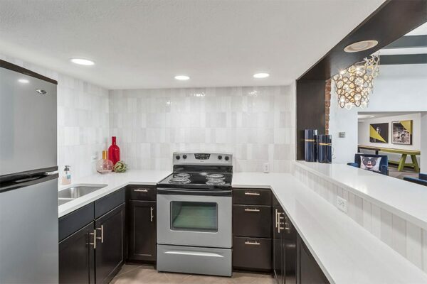 Community kitchen with wood cabinets, tiled walls, stainless steel appliances, and breakfast bar.