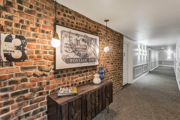 Hallway with carpet, brick accent wall, brass pendant lights, and eclectic decor.