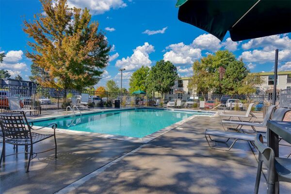 Fenced pool area with lounge chairs and tall trees.