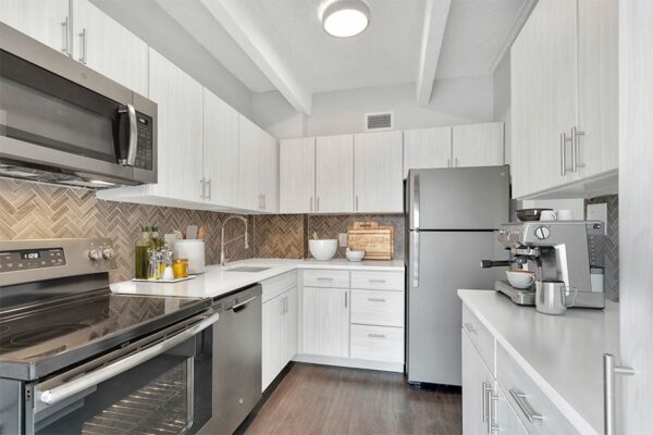 Kitchen with wood floor, white cabinets and counters, stainless steel appliances, and tiled backsplash.