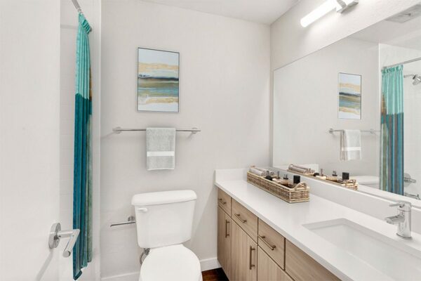 Bathroom with wood cabinets, white counters and sink, large mirror, and abstract artwork.