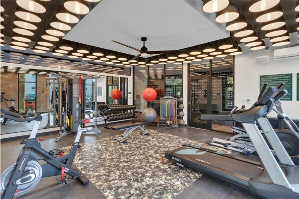 Fitness center with storage cubbies, cardio machines, weight equipment, and large ceiling fan.