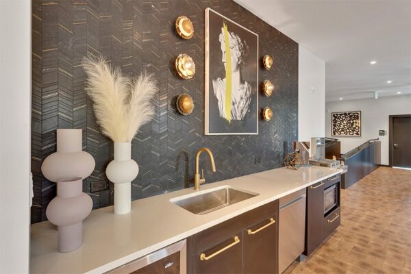 Community kitchen with stainless steel appliances, white counter, bronze fixtures, and modern artwork.