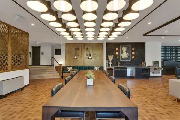 Lounge with community kitchen, large wood dining table with leather chairs, dense lighting fixture, and decorative wall panels.